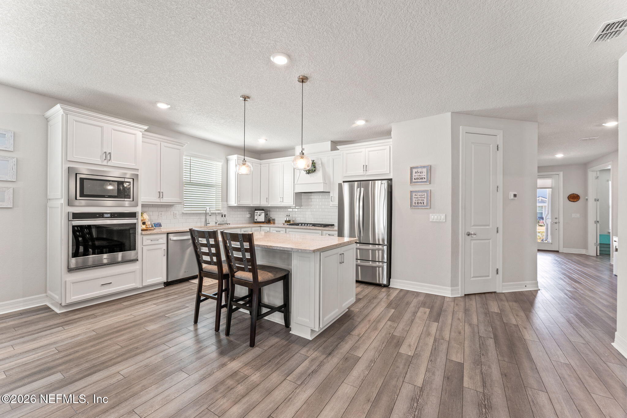 345 Muhly Grass Street Yulee, FL 32097 - Photo 11 of 42 a kitchen with stainless steel appliances a refrigerator a stove top oven a sink dishwasher and a dining table with wooden floor