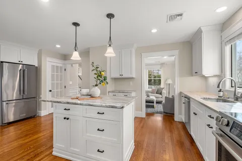 a kitchen with stainless steel appliances kitchen island granite countertop a sink a stove a refrigerator and a wooden floor