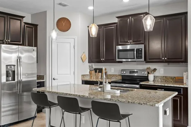 a kitchen with stainless steel appliances granite countertop a sink a stove a refrigerator cabinets and chairs