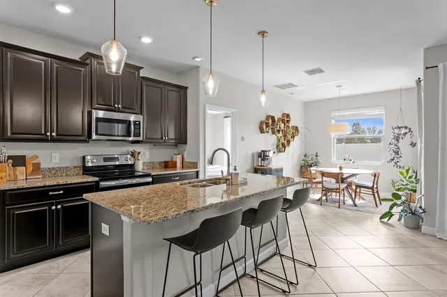 a kitchen with granite countertop a stove a sink a refrigerator a dining table and chairs