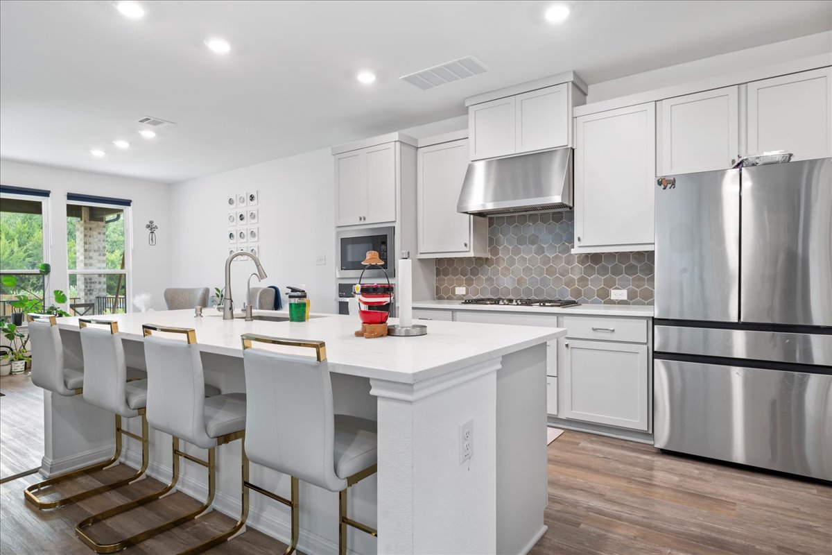 209 Terra Mnr Trail Georgetown, TX 78628 - Photo 10 of 40 Kitchen with stainless steel appliances, decorative backsplash, under cabinet range hood, an island with sink, and a breakfast bar