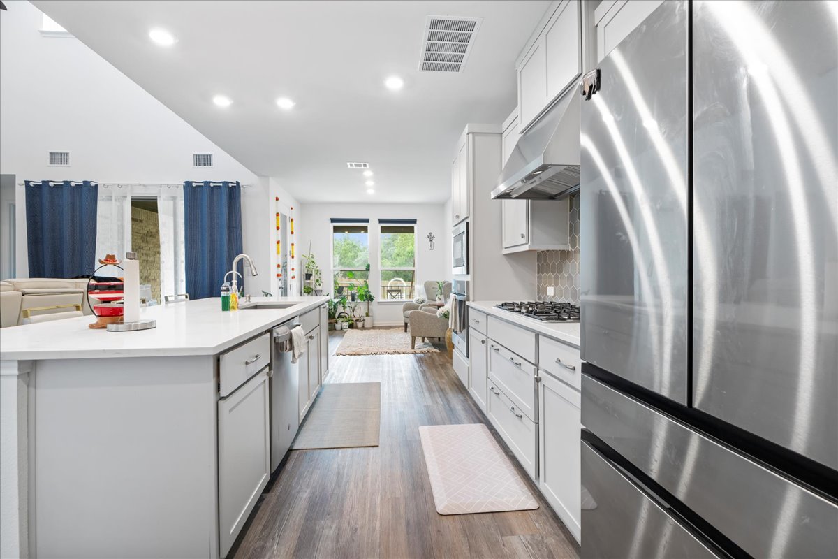 209 Terra Mnr Trail Georgetown, TX 78628 - Photo 40 of 40 Kitchen featuring appliances with stainless steel finishes, open floor plan, white cabinetry, dark wood-style floors, and an island with sink