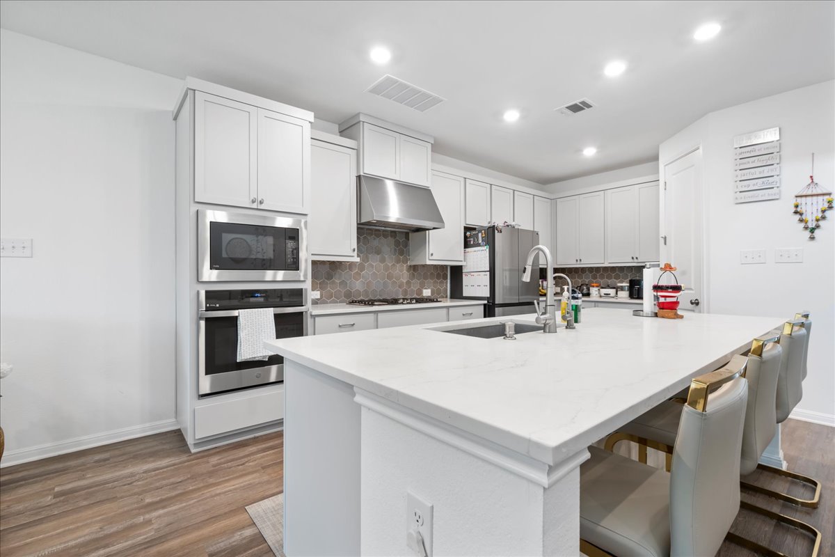 209 Terra Mnr Trail Georgetown, TX 78628 - Photo 14 of 40 Kitchen with stainless steel appliances, a breakfast bar area, an island with sink, light stone countertops, and tasteful backsplash