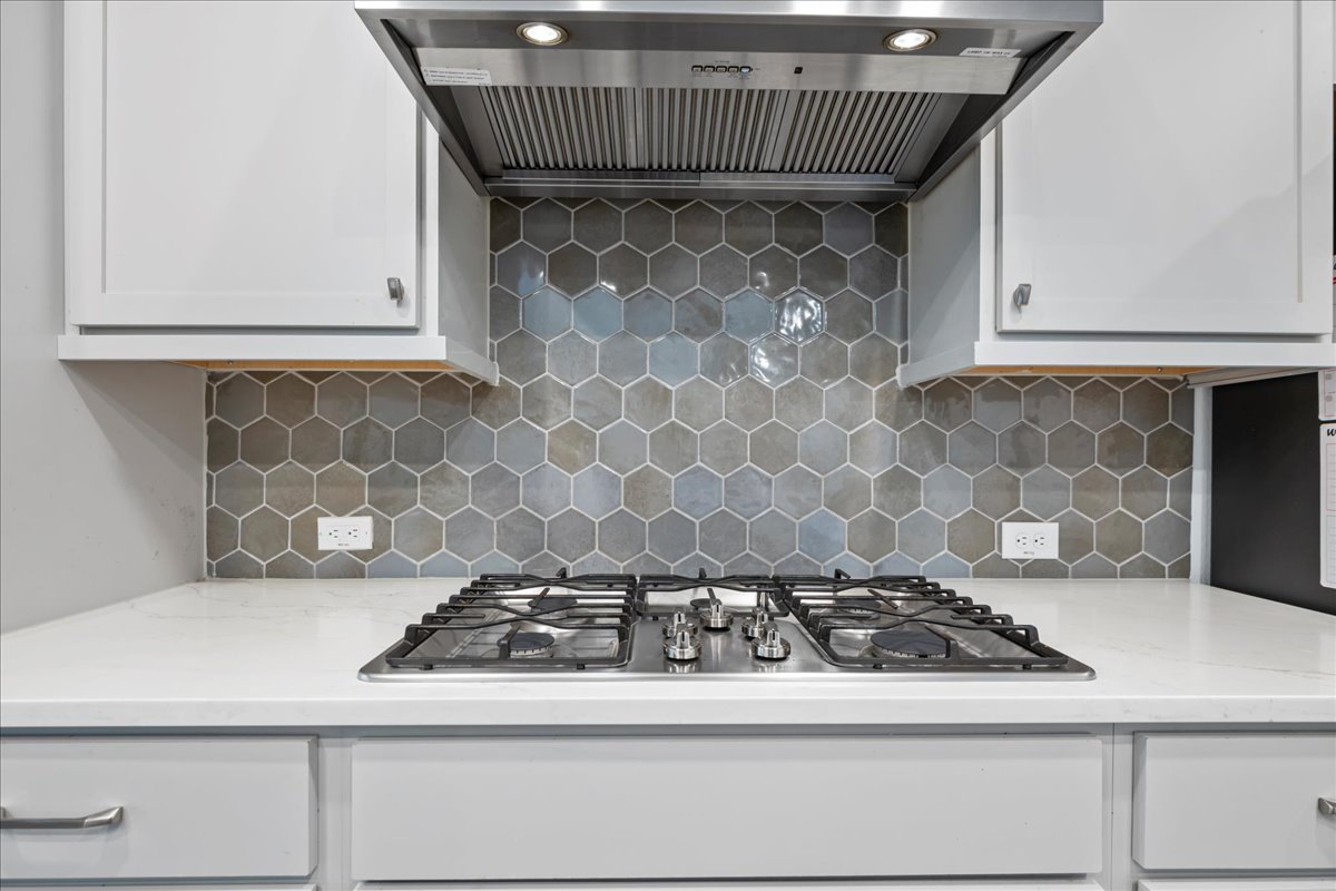 209 Terra Mnr Trail Georgetown, TX 78628 - Photo 7 of 40 Kitchen with wall chimney range hood, stainless steel gas cooktop, light stone counters, and white cabinets