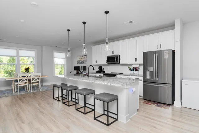 a kitchen with stainless steel appliances a stove a sink a refrigerator a table and chairs with wooden floor