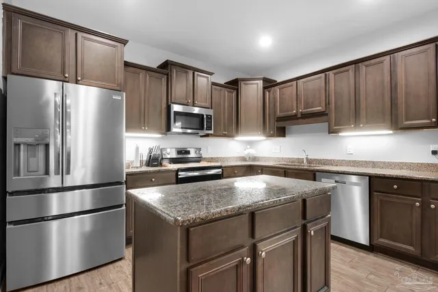 a kitchen with kitchen island granite countertop wooden cabinets a refrigerator and a sink