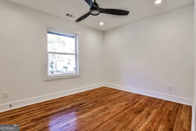 an empty room with wooden floor ceiling fan and windows