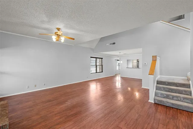 a view of an empty room with wooden floor and a ceiling fan