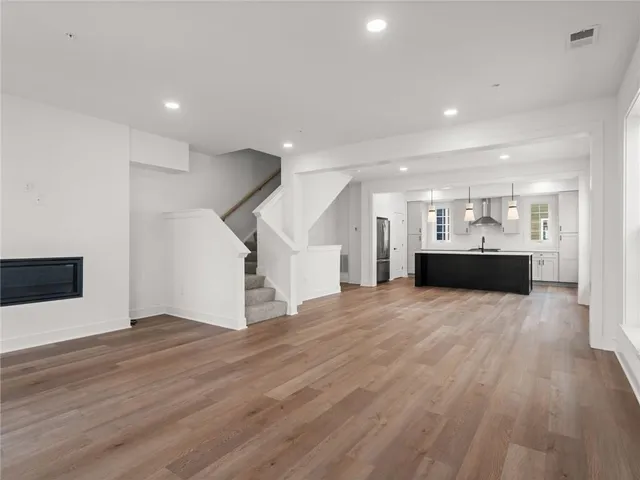 a view of an empty room with wooden floor and kitchen view
