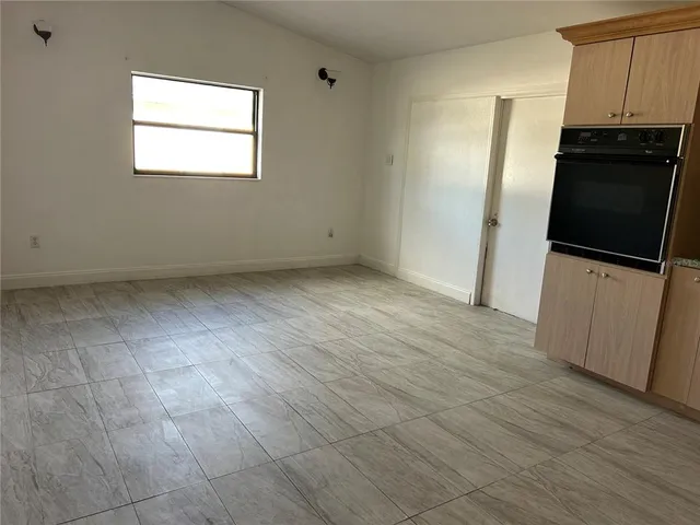 a view of a refrigerator in kitchen and an empty room with wooden floor