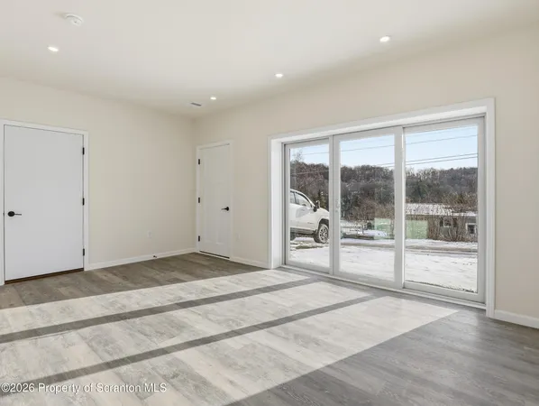 a view of an empty room with wooden floor and windows
