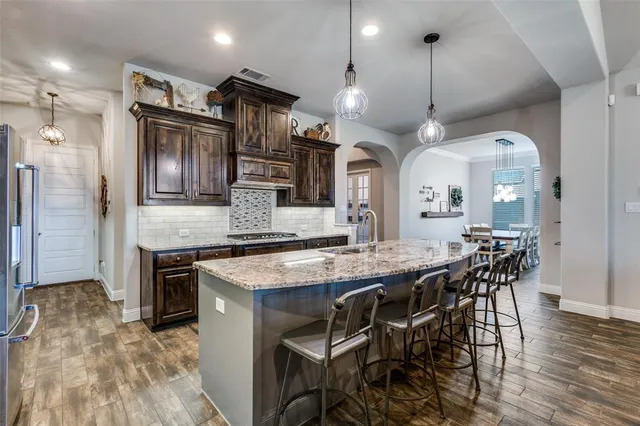 a kitchen with stainless steel appliances kitchen island granite countertop a table chairs sink and wooden floor