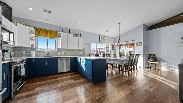 a kitchen with stainless steel appliances granite countertop a stove top oven a sink a dining table and chairs with wooden floor