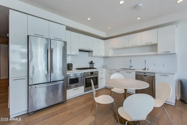 a kitchen with stainless steel appliances granite countertop a refrigerator a stove a sink dishwasher a dining table and chairs with wooden floor