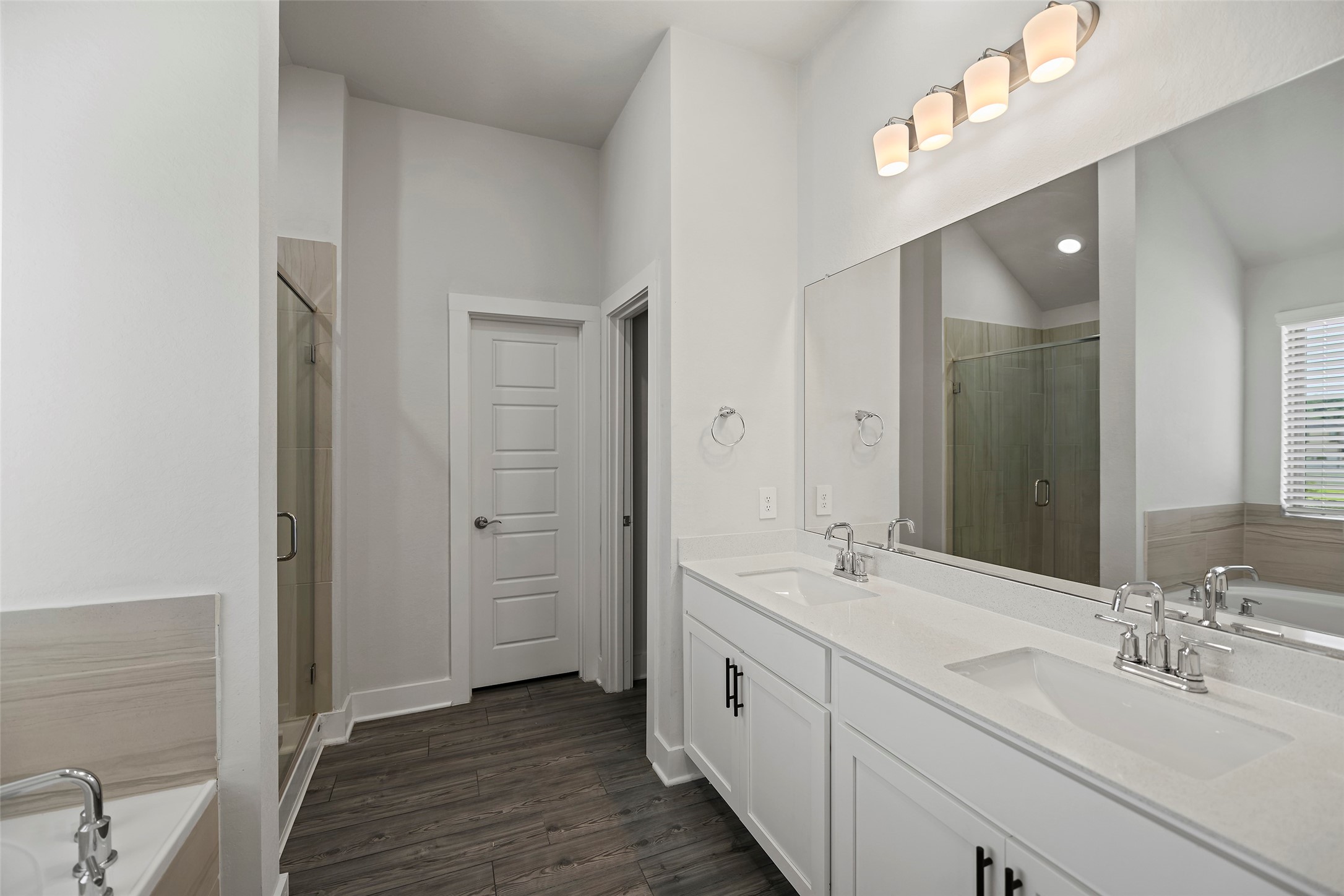 10603 Whitejacket Conroe, TX 77385 - Photo 17 of 42 Primary bathroom features a modern design with dual sinks, a large mirror, elegant lighting, and a glass-enclosed shower. The neutral color palette and wood-style flooring create a clean and inviting atmosphere.