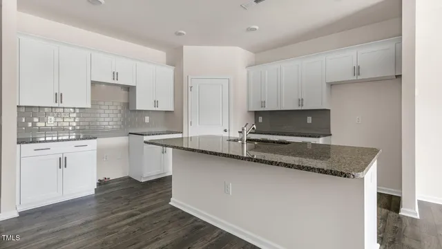 a kitchen with stainless steel appliances granite countertop a sink dishwasher a refrigerator and white cabinets with wooden floor