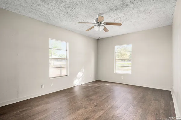 an empty room with wooden floor fan and windows