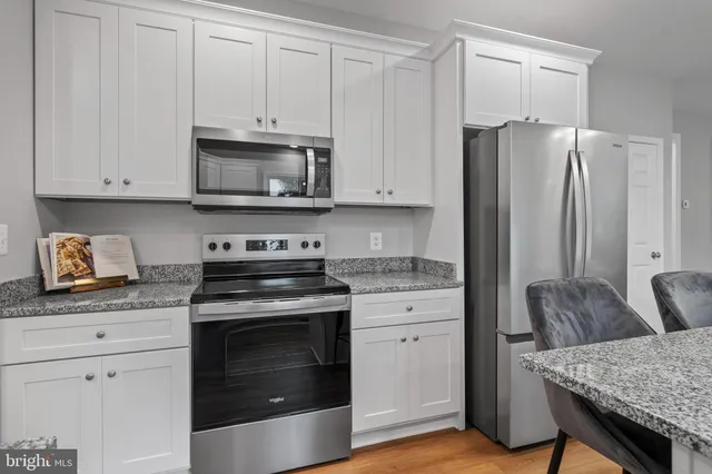 a kitchen with granite countertop a stove a sink and a refrigerator with white cabinets