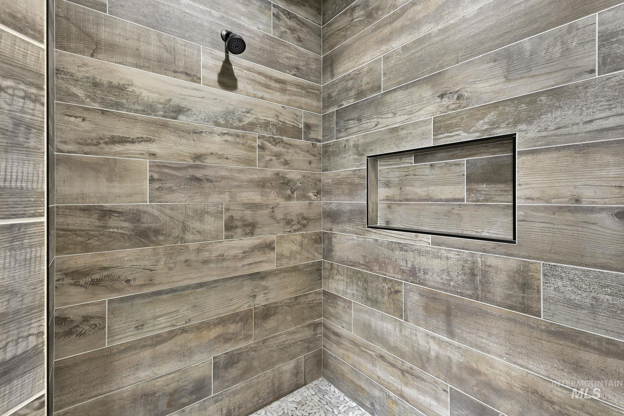 5676 East Zaffre Ridge Street Boise, ID 83716 - Photo 30 of 50 Shower enclosure featuring wood-look tile walls, a built-in shower niche, a matte black shower head, and a pebble tile floor