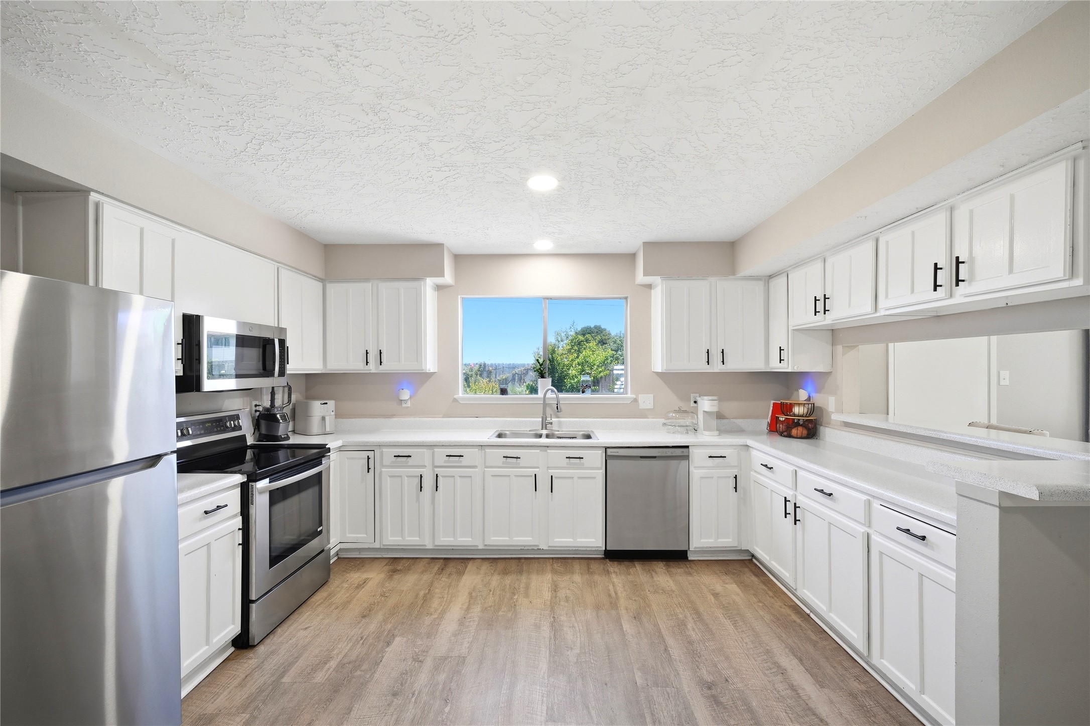 4718 Temple Bell Drive Spring, TX 77388 - Photo 21 of 50 This modern kitchen features stainless steel appliances, ample white cabinetry, and a bright, open layout with a central window view, complemented by sleek wood-style flooring.