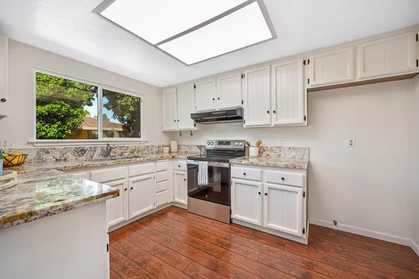 a kitchen with stainless steel appliances granite countertop a stove top oven a sink a dining table and chairs with wooden floor