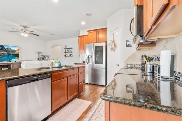 a kitchen with stainless steel appliances granite countertop a refrigerator a sink dishwasher a stove and white countertops with wooden floor