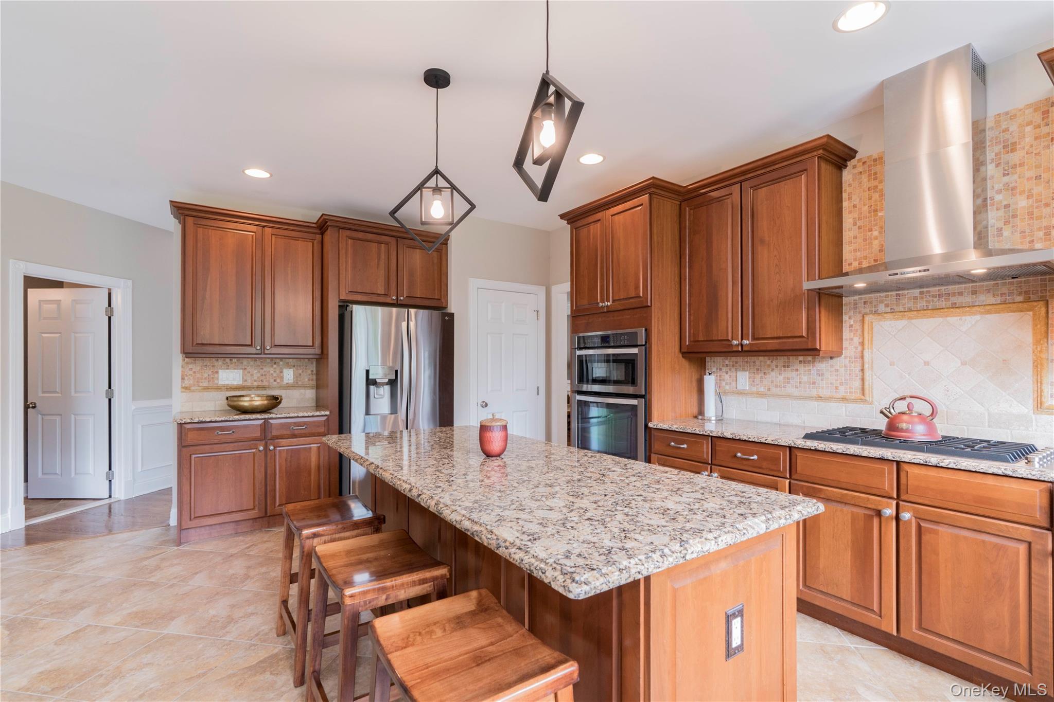 78 Moore Road Hopewell Junction, NY 12533 - Photo 13 of 38 Kitchen with wall chimney range hood, backsplash, brown cabinetry, hanging light fixtures, and a kitchen breakfast bar