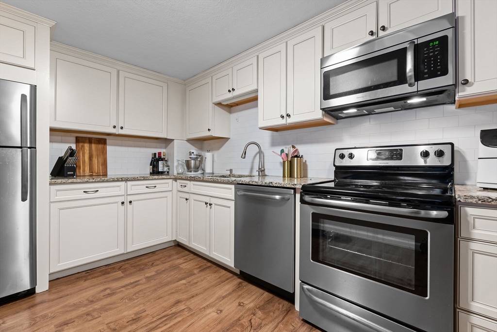 9 Broadway, Unit 210 Saugus, MA 01906 - Photo 11 of 24 a kitchen with cabinets stainless steel appliances and a wooden floor