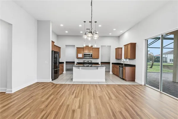 a large kitchen with stainless steel appliances kitchen island granite countertop a refrigerator oven a sink dishwasher a dining table and chairs with wooden floor
