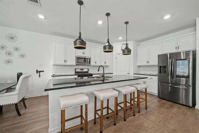 a kitchen with stainless steel appliances granite countertop a sink a stove a refrigerator and chairs