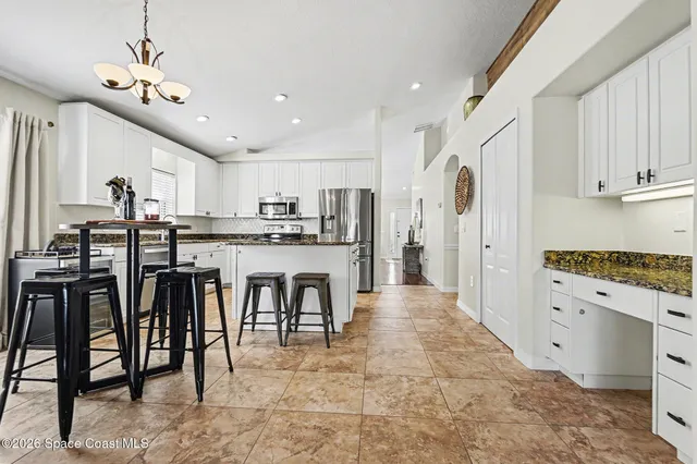 a kitchen with stainless steel appliances kitchen island granite countertop a table chairs refrigerator and cabinets