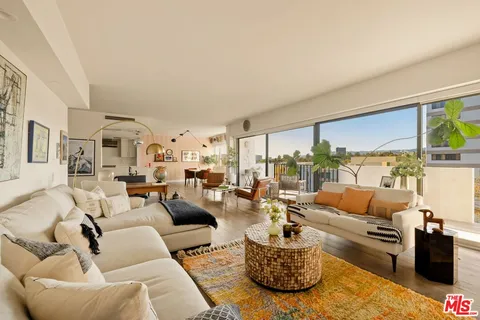 a living room with furniture large windows and a view of kitchen