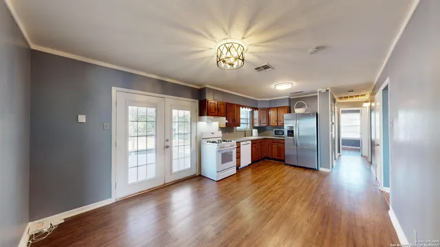 a large kitchen with stainless steel appliances granite countertop a refrigerator a stove a sink dishwasher a dining table and chairs with wooden floor