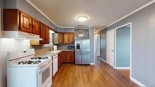 a kitchen with stainless steel appliances granite countertop a refrigerator a sink dishwasher a stove and white countertops with wooden floor