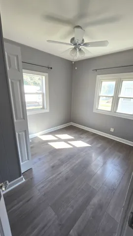 an empty room with wooden floor fan and windows