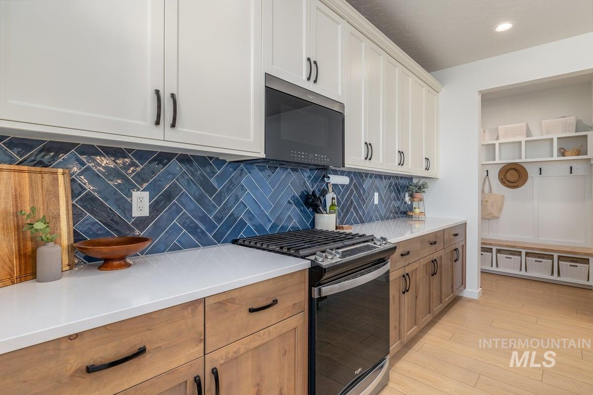 1380 West Chilitna Street Meridian, ID 83642 - Photo 10 of 50 Kitchen featuring white upper cabinetry, wood-finish lower cabinetry, a white countertop, a blue herringbone tile backsplash, and a black range with an overhead microwave