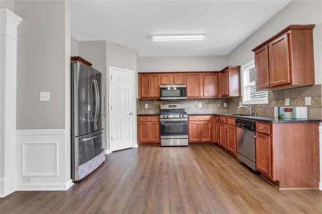 a kitchen with stainless steel appliances granite countertop a refrigerator oven a sink dishwasher and wooden cabinets with wooden floor