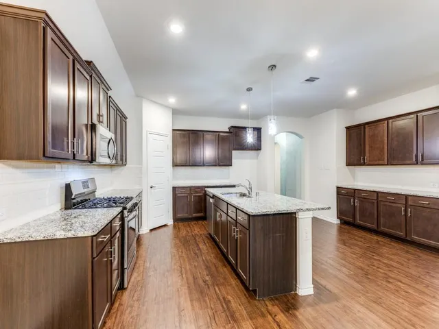 a kitchen with stainless steel appliances granite countertop wooden cabinets a sink dishwasher a stove and a refrigerator
