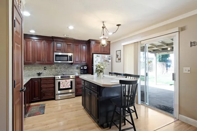 a kitchen with kitchen island granite countertop a stove top oven a sink dishwasher a dining table and chairs with wooden floor