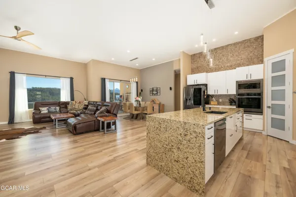 a large kitchen with stainless steel appliances kitchen island granite countertop a refrigerator a stove a sink and white cabinets with wooden floor