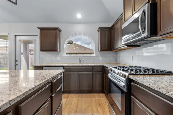 a kitchen with granite countertop a sink dishwasher stove and cabinets with wooden floor