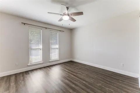 an empty room with wooden floor chandelier fan and windows
