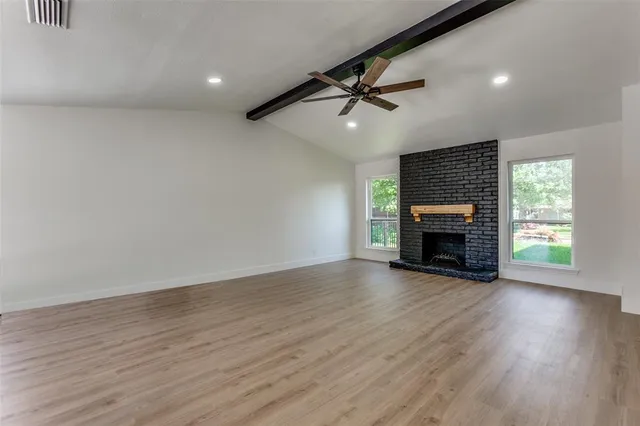 an empty room with wooden floor fireplace and windows