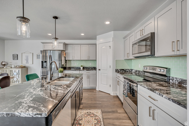 1577 Quailhill Road Saratoga Springs, UT 84045 - Photo 13 of 46 Kitchen with stainless steel appliances, decorative light fixtures, dark stone counters, light wood-style floors, and a kitchen island with sink