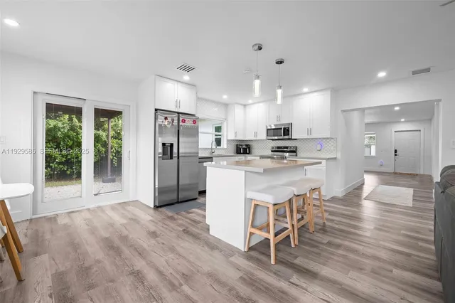 a kitchen with stainless steel appliances granite countertop a refrigerator a oven a sink and white cabinets with wooden floor