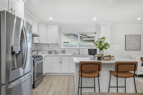a kitchen with stainless steel appliances a dining table chairs refrigerator and sink