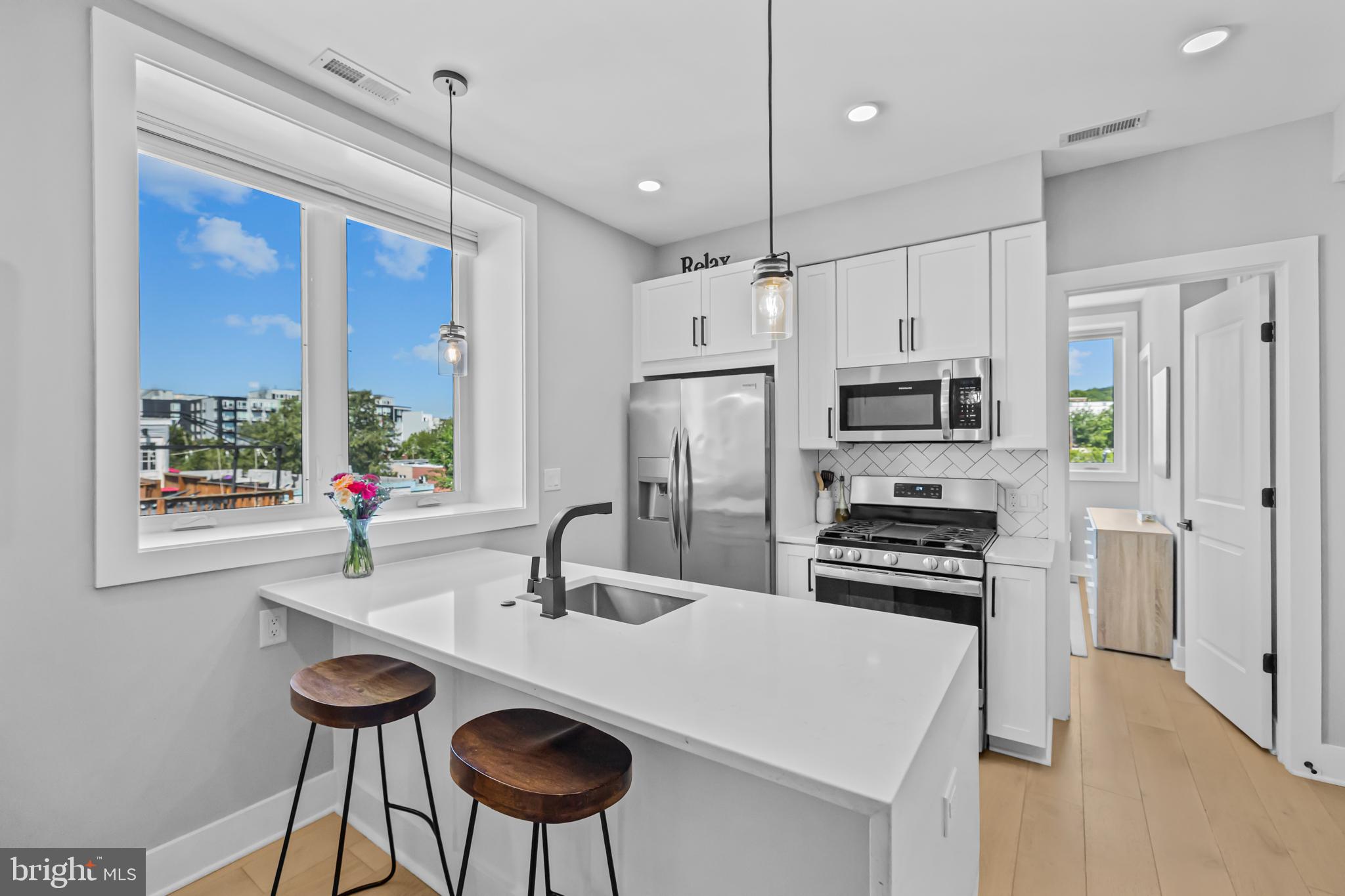 1915 H Street Northeast, Unit PH1 Washington, DC 20002 - Photo 8 of 21 a kitchen with stainless steel appliances a sink a stove a refrigerator a dining table and chairs