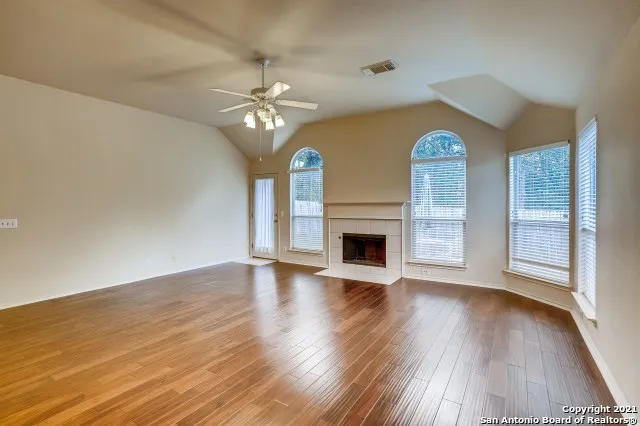 an empty room with wooden floor fireplace and windows