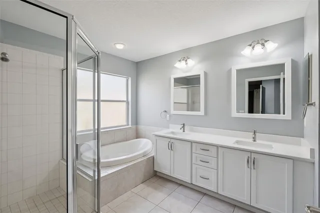 a bathroom with a double vanity sink a mirror a bathtub and next to a window