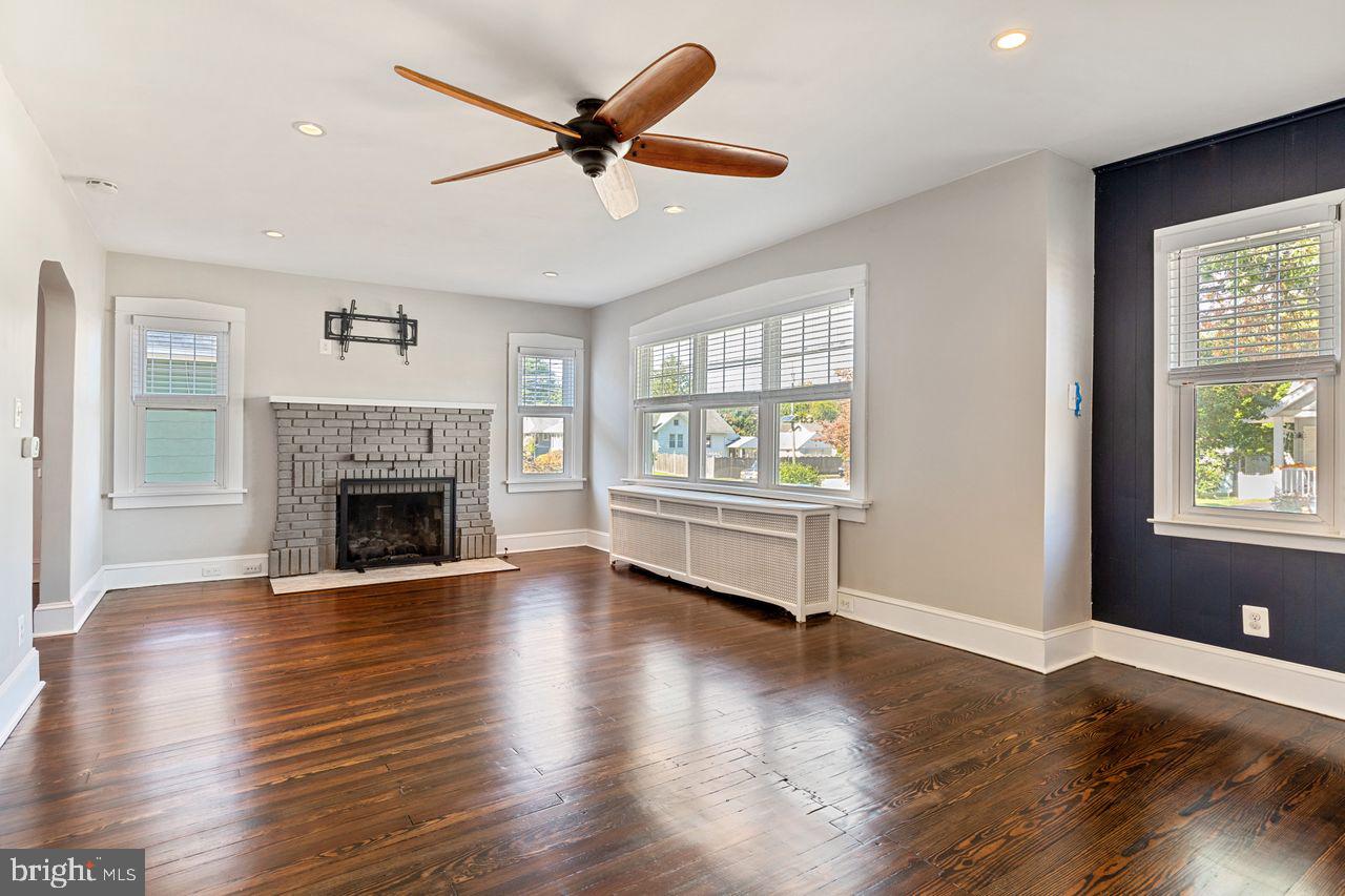 204 Princeton Road Audubon, NJ 08106 - Photo 2 of 22 an empty room with windows a fireplace a ceiling fan and wooden floor
